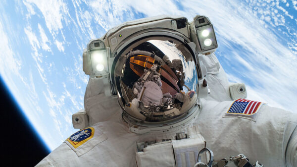 A NASA astronaut above with the Earth behind them and the ISS reflected in their helmet visor