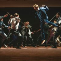Men in suits charge at one another as thought they're on a medieval battlefield, wielding swords