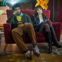 A man and woman are sat on a small armchair looking at a screen we can't see as a projector beams behind them