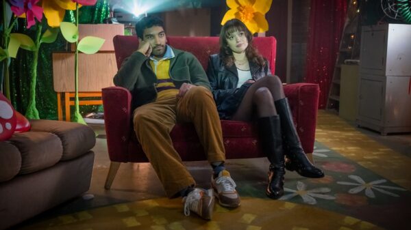A man and woman are sat on a small armchair looking at a screen we can't see as a projector beams behind them