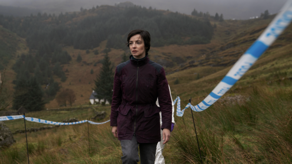 A character climbs up a hill covered in police tape, a still taken from The Dark